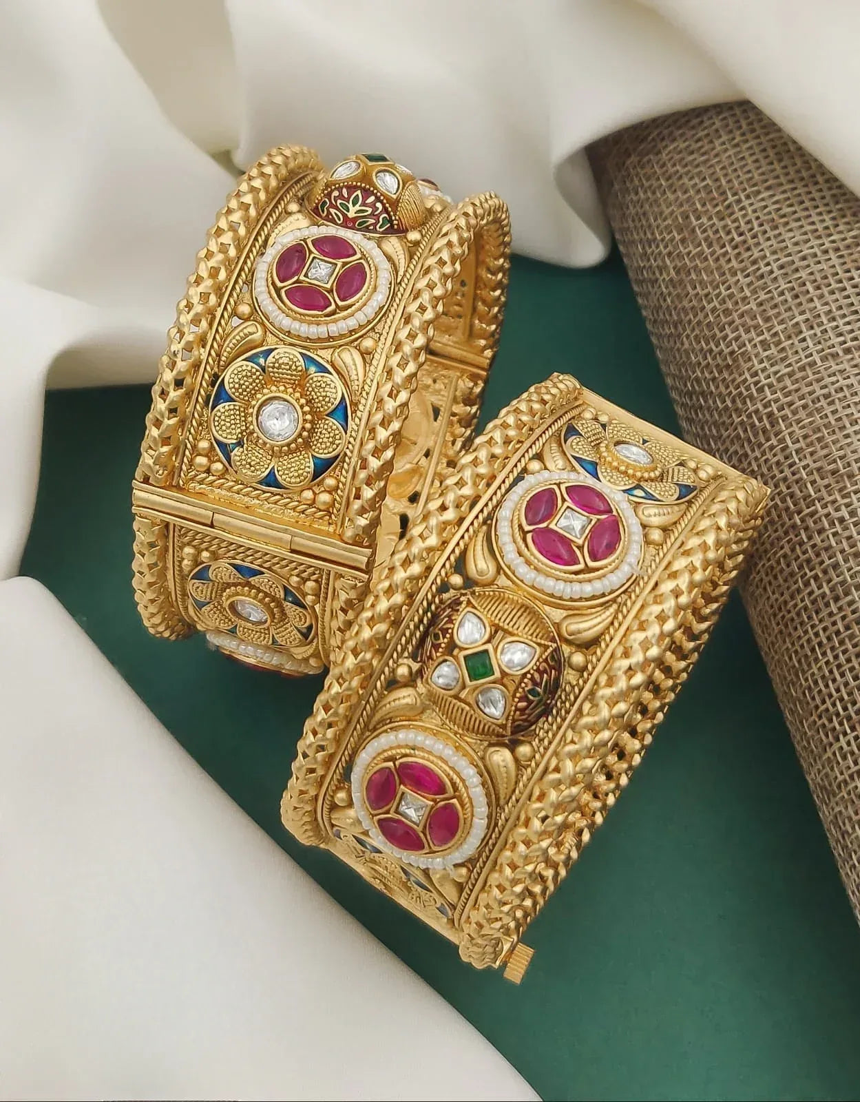 Pair of ornate gold bangles with red, green, white stones and intricate floral designs