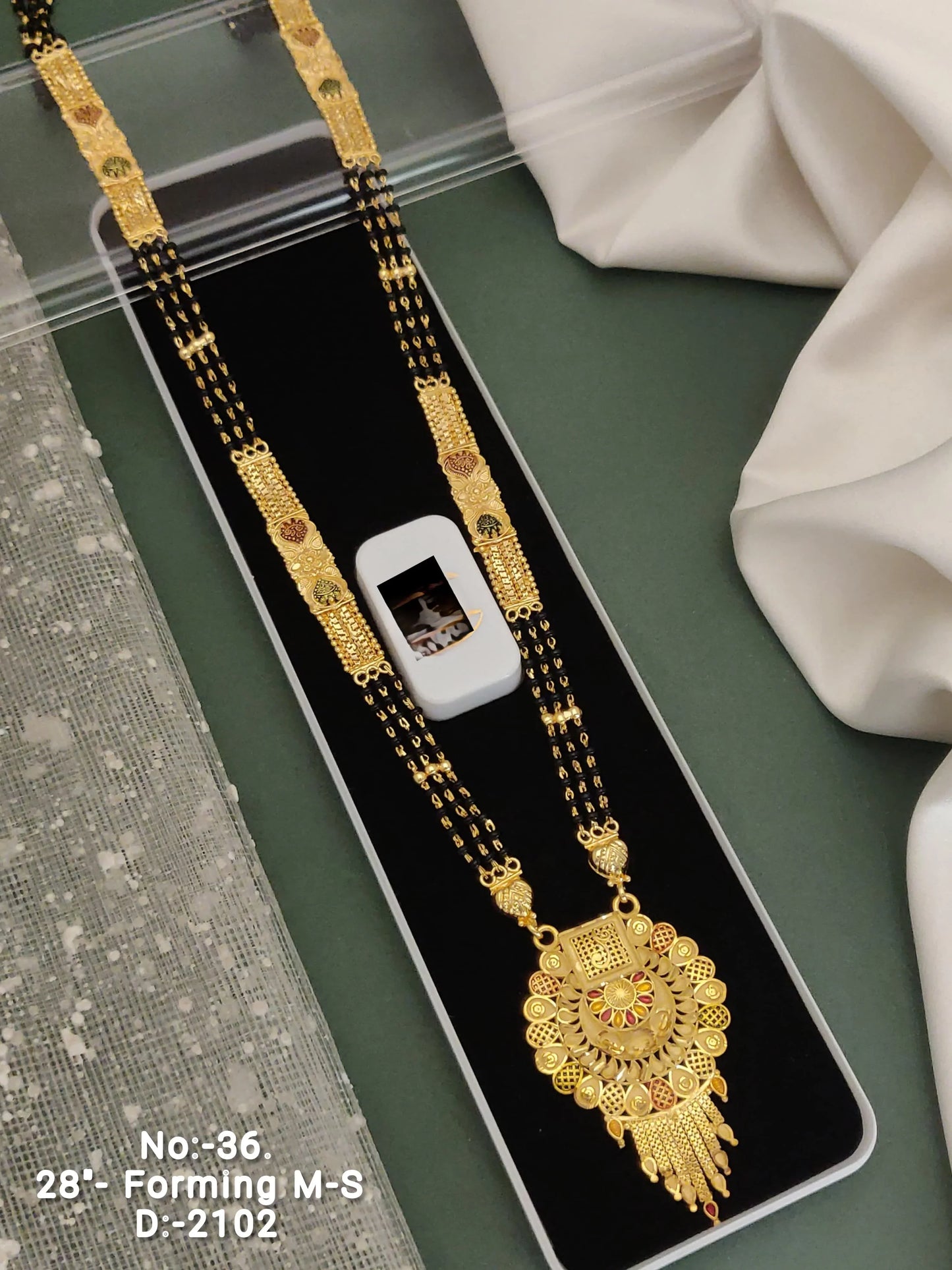 Gold mangalsutra necklace with intricate pendant on black velvet tray and white fabric background
