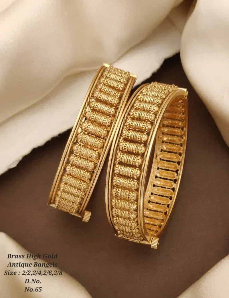 Antique high gold brass bangles with intricate cylindrical patterns on beige fabric