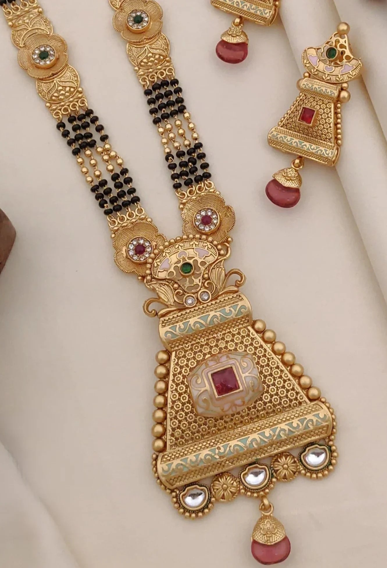 Traditional gold necklace and earrings set with intricate designs, red and green stones, and black beads