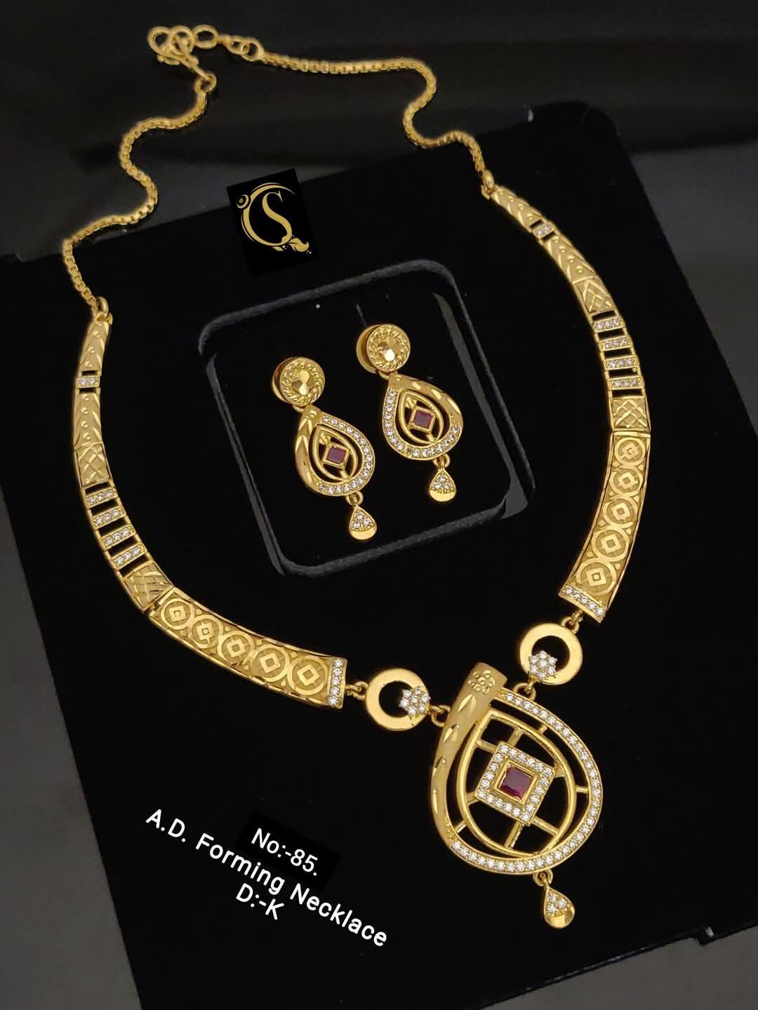 Gold AD forming necklace and matching earrings with intricate designs and red stone accents on black background