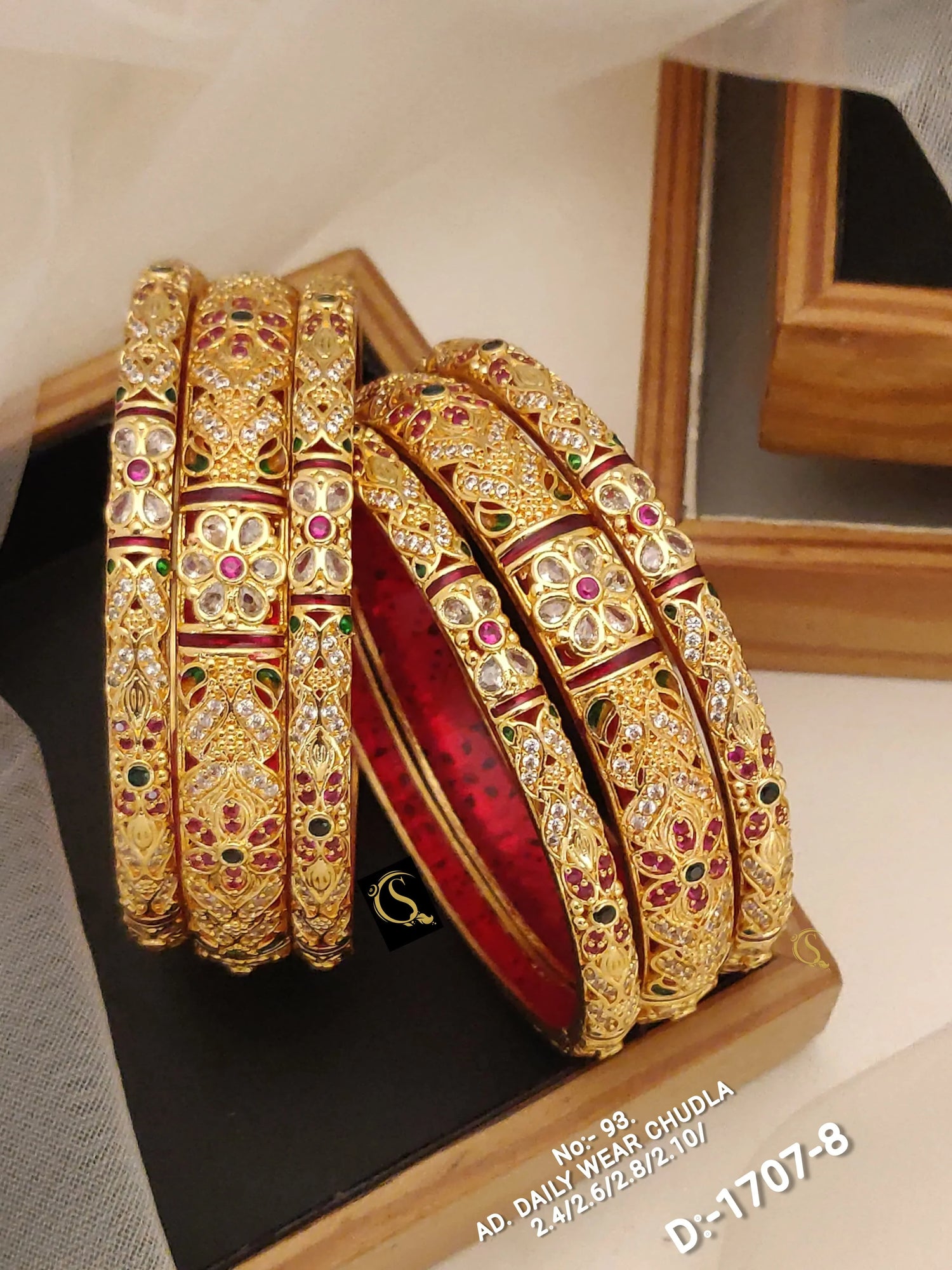Set of six gold daily wear bangles with floral patterns and red, green gemstone accents on black and wooden stand
