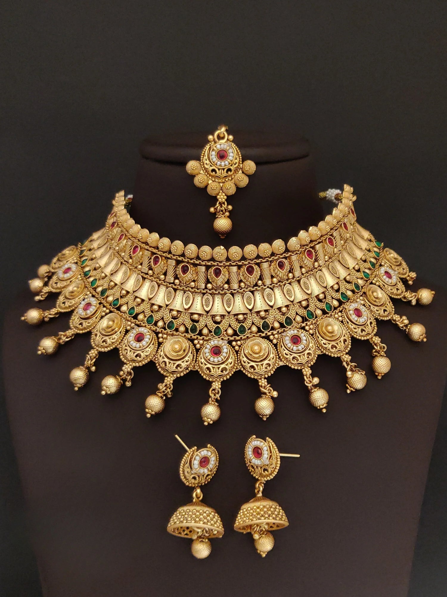 Intricate gold traditional necklace set with red and green gemstone accents and matching earrings