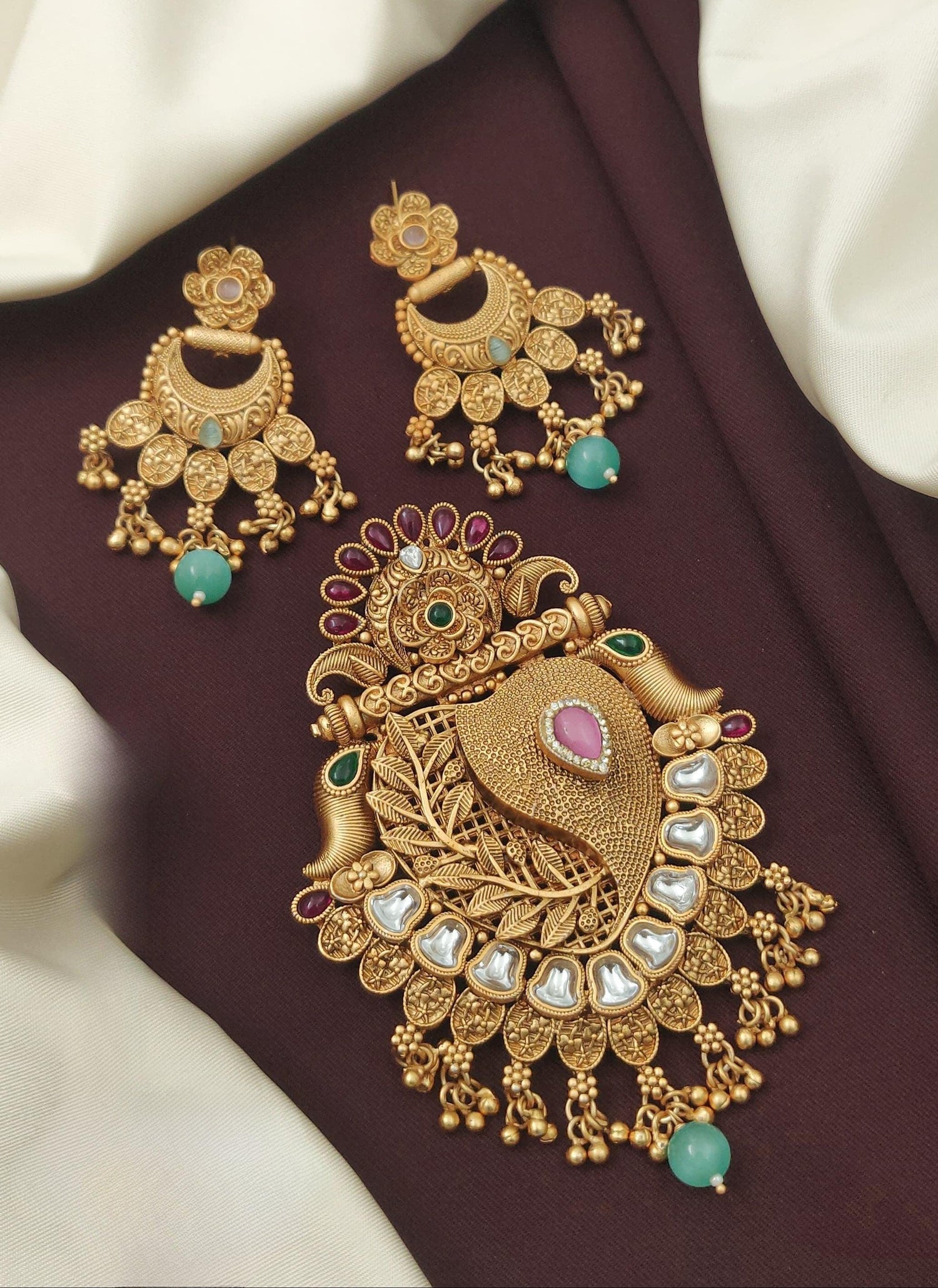 Intricate gold jewelry set with green and pink stones on brown and cream fabric background