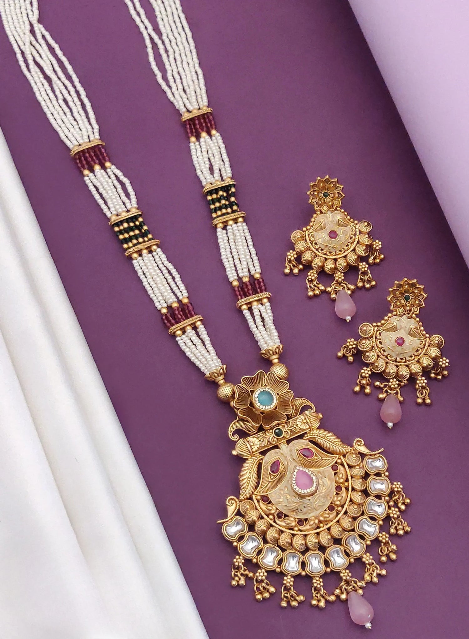 Traditional gold-tone necklace with intricate pendant and matching earrings featuring pearls and pink stones on purple background