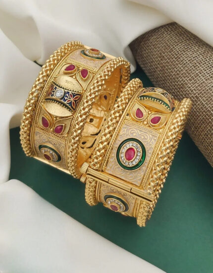 Intricate gold bangles with red and white gemstones and detailed floral patterns on green and beige fabric